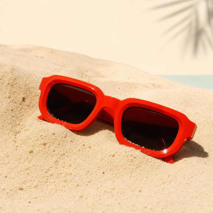 Gafas de sol rojas medio enterradas en la arena